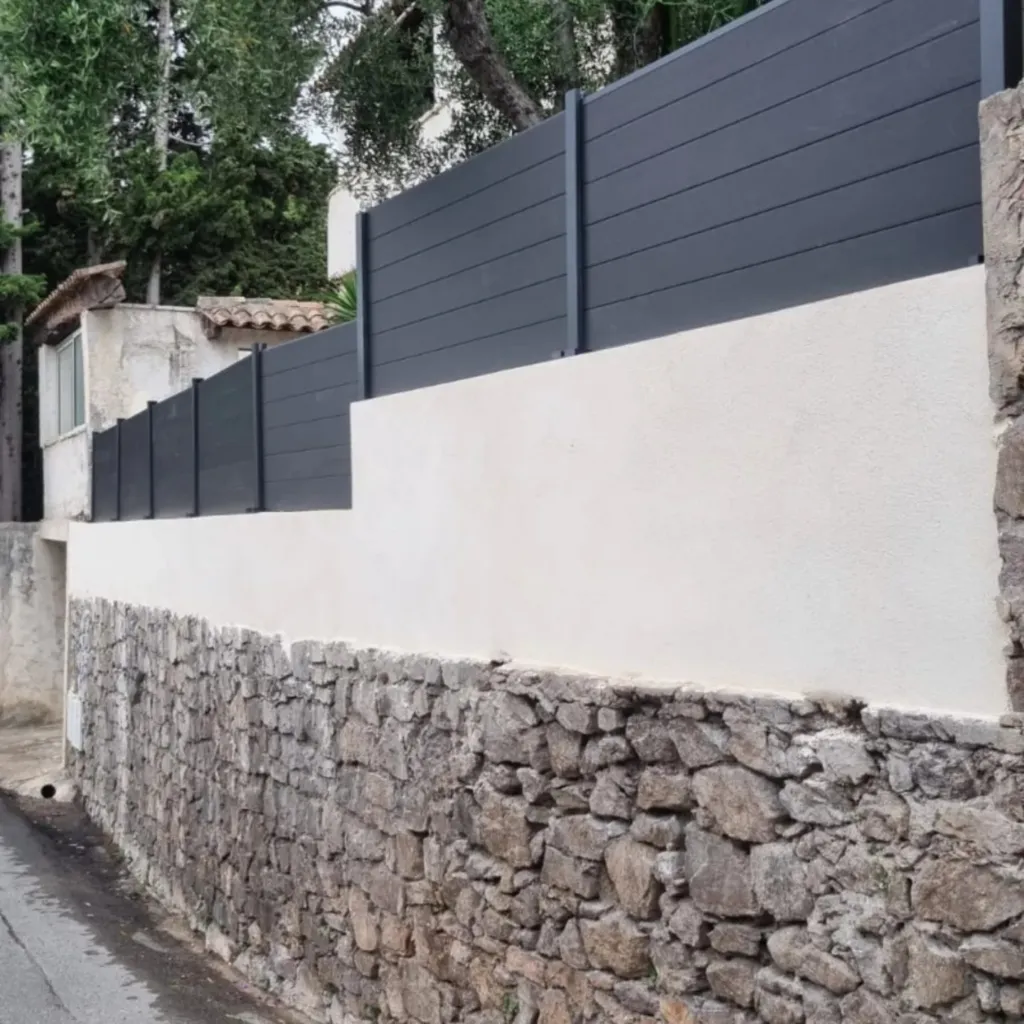 Muret en pierre apparente surmonté d'un mur enduit clair et d'une clôture aluminium gris anthracite.