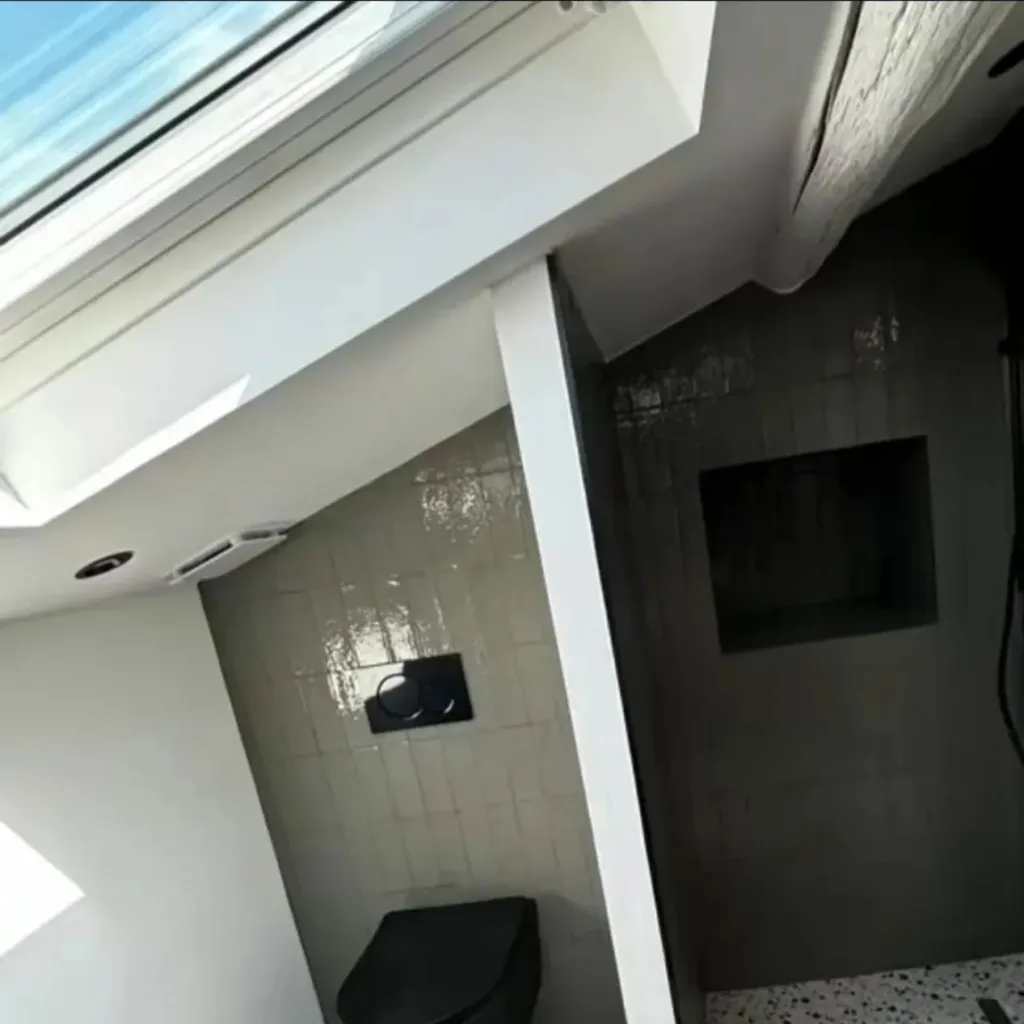 Salle d'eau sous velux avec douche à l'italienne, robinetterie noire, niche carrelée et WC suspendu noir.