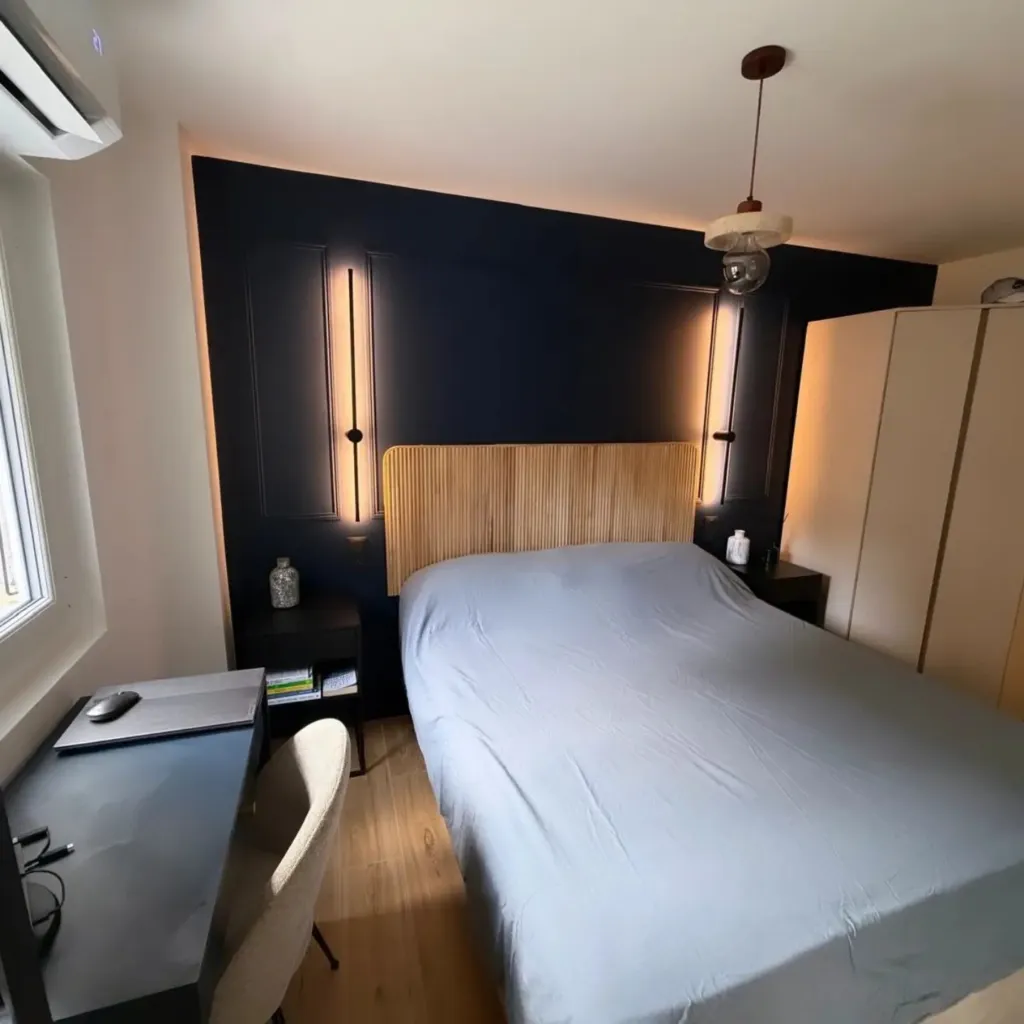 Chambre avec panneau mural noir, tête de lit à tasseaux bois, appliques LED verticales et dressing.
