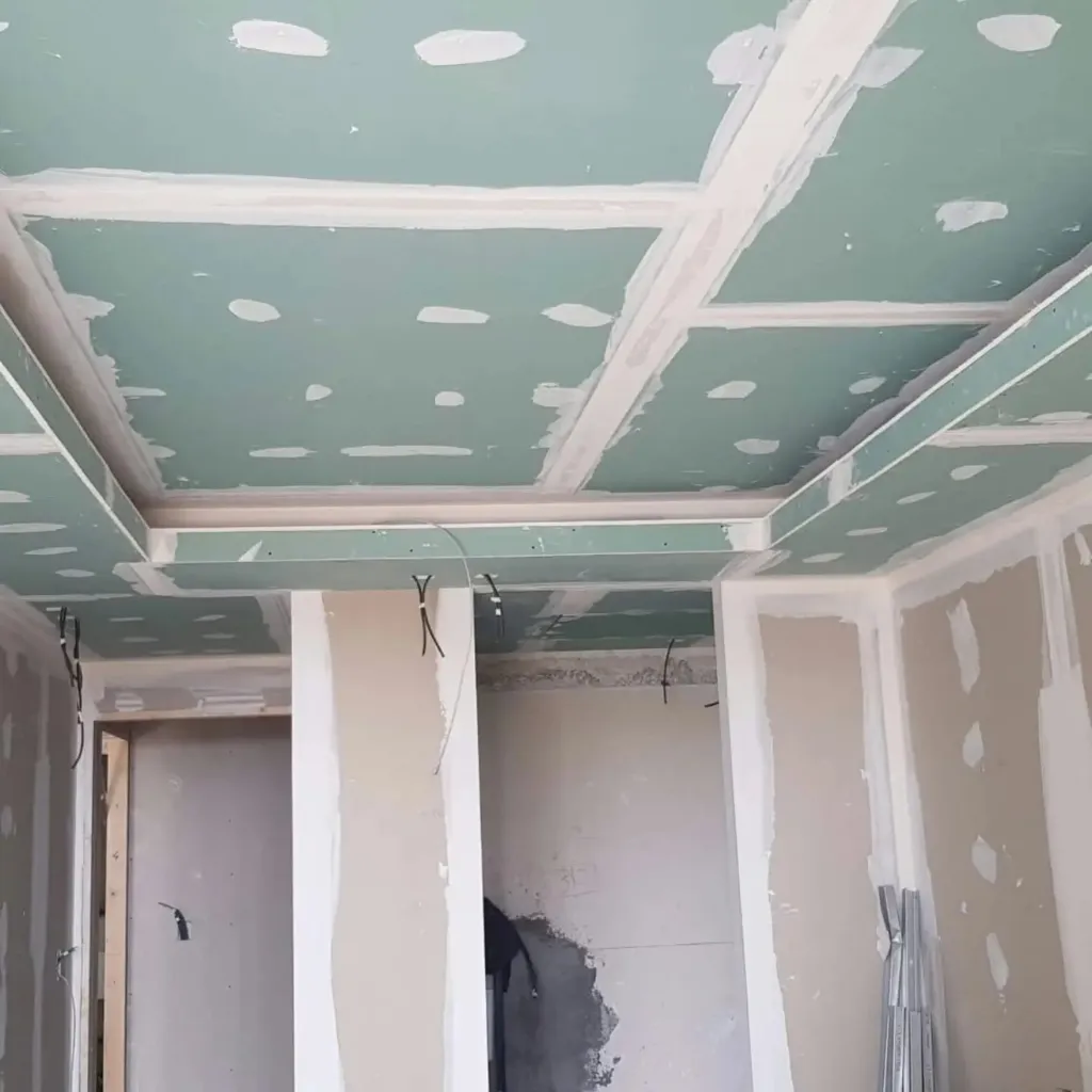Plafond en plaques de plâtre avec bandes à joints enduites et retombées périphériques, ossature de cloisons au fond.