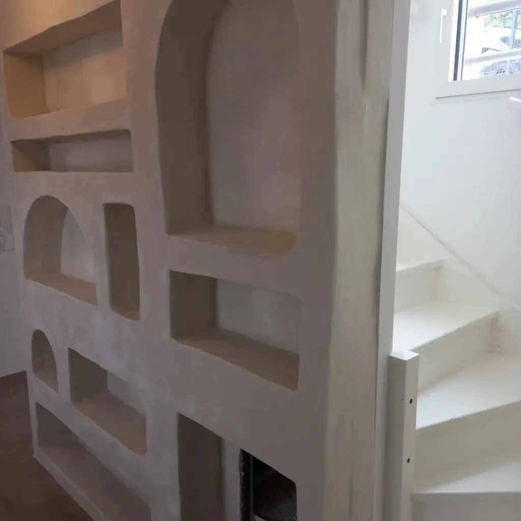 Gros plan sur les niches arrondies d'un mur en plâtre à côté d'un escalier blanc.