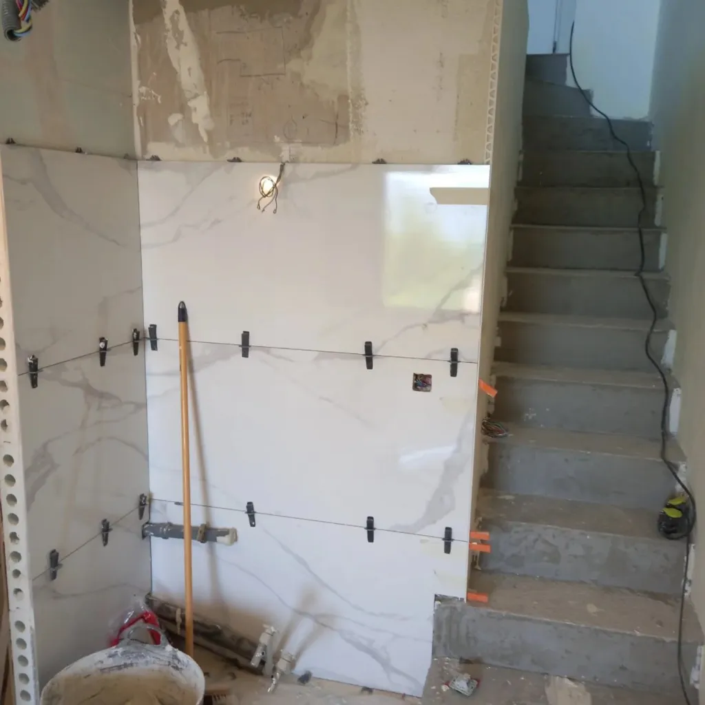 Pose de grand panneau de grès cérame effet marbre blanc sur un mur avec croisillons, clips de mise à niveau et escalier en béton.