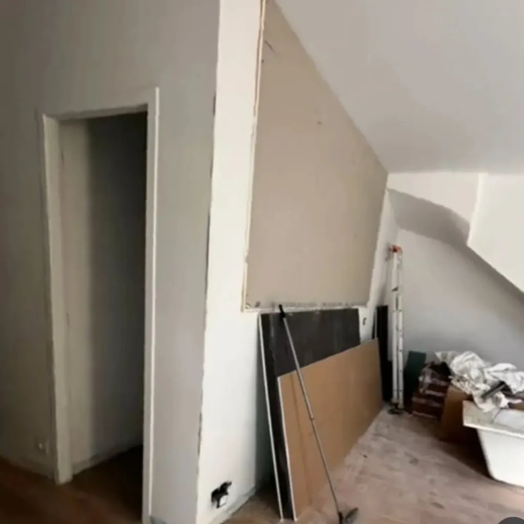 Cloison en plaque de plâtre posée sous une toiture en pente avec encadrement de porte, chantier en cours.