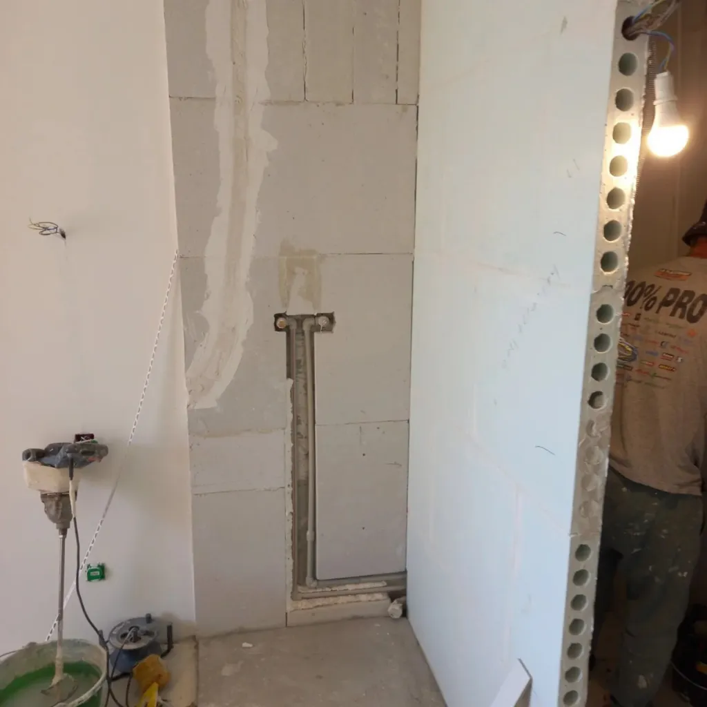 Mur en béton cellulaire avec attentes d'alimentation encastrées pour une douche et seau de colle en chantier.