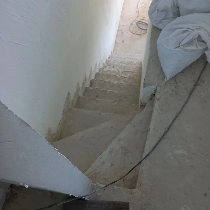 Escalier intérieur en béton brut après dépose du revêtement, câble au sol et bâches blanches.
