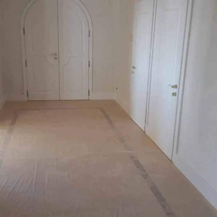 Couloir aux murs blancs avec portes cintrées et sol en marbre recouvert d'une bâche.
