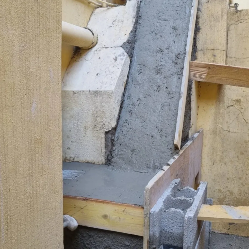 Réparation d'un ressaut de façade au mortier avec coffrage bois et parpaing, conduit horizontal en haut.