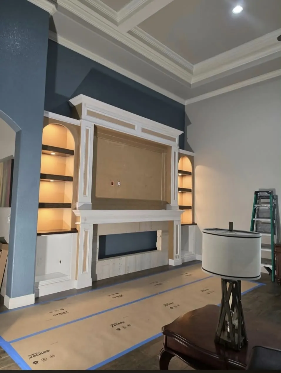 A built-in white entertainment center with illuminated arched shelving against a blue wall during a room renovation